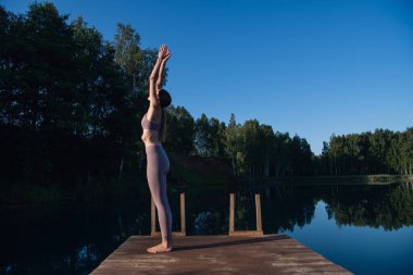 Gün doğumunda gökyüzüne karşı yoga yapan genç bir kadın. Oldukça zayıf bir kadın egzersiz yapıyor. Sağlık, meditasyon, sağlık, farkındalık konsepti.