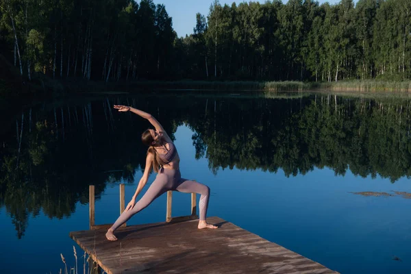 Orman gölünde yoga yapan bir kadın. Dışarıda esneme ve esneklik egzersizleri yapan güzel bir kız.