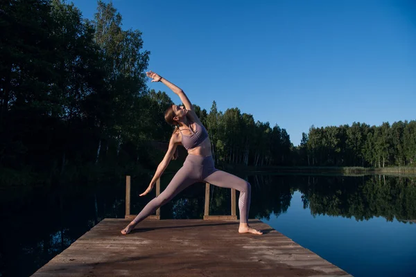 Красива молода жінка виконує духовну позу йоги на лісовому озері в сонячний день, схід сонця дзен оздоровлення — стокове фото