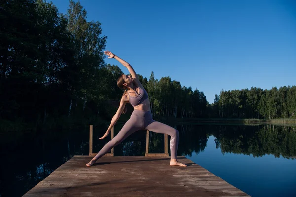 Gyönyörű fiatal nő végez spirituális jóga pózt egy erdei tavon napsütéses napon, napkelte zen wellness — Stock Fotó