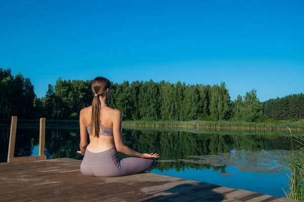 Healthy woman practicing yoga on the lake at sunrise enjoying positive energies from nature — Stock Photo, Image