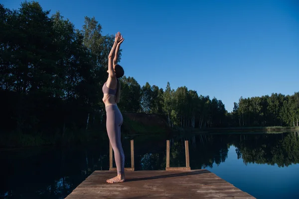 Mujer joven practicando yoga contra el cielo al amanecer. Mujer bastante delgada realiza un ejercicio. Salud, meditación, bienestar, concepto de atención plena. — Foto de Stock