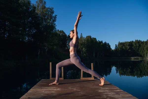 Ragazza sta praticando la tecnica dello yoga sul molo vicino al lago e meditando. Meditazione per purificare la mente e la calma. Immagini Stock Royalty Free