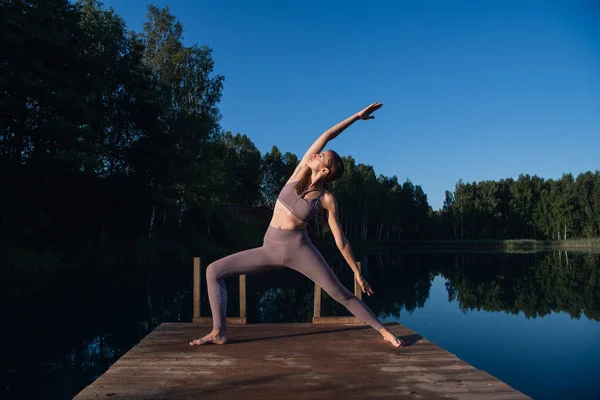 Donna sana praticare yoga sul lago all'alba godendo di energie positive dalla natura Immagini Stock Royalty Free