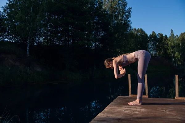 Девушка практикует технику йоги на пирсе у озера и медитирует. Медитация для очищения ума и спокойствия. Стоковая Картинка