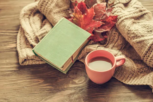 Autumn morning coffee. A cup of coffee on a wooden table and a warm sweater on a background of autumn leaves. Still life concept. Copy space.