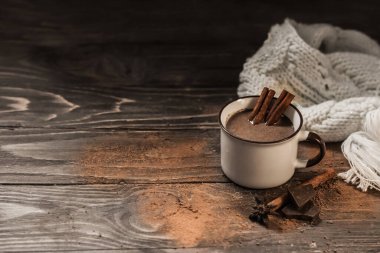 Bir kupa sıcak çikolata ya da ahşap bir masanın üzerinde tarçın çubukları olan kakao. Sıcak eşarp ve sıcak sonbahar kış konsepti.