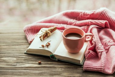 Sabah kahvesi. Konforlu kompozisyon: Ahşap bir masada bir fincan kahve ve sıcak bir kazak, açık bir kitap. Hayat konsepti. Boşluğu kopyala. 