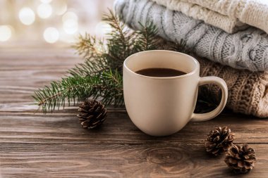 Sabah kahvesi. Isınan bir içecek, köknar dalları ve örgü kazakların arka planında koniler. Kopya alanı olan ahşap bir arkaplan. İç kısımda kış dekorasyonu.