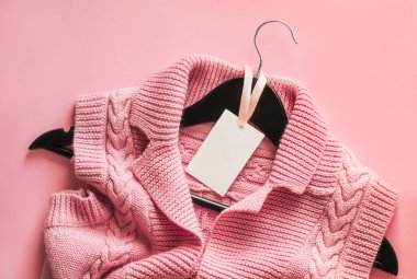 Elbise etiketi, tasarımını yerleştirmek için boş etiket şablonu. Pembe arka planda siyah ahşap bir askıya örülmüş pembe bir yelek. Bir giyim mağazası için reklam pankartı..