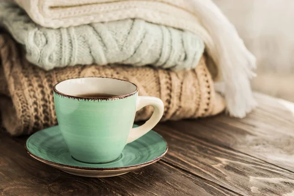 stock image A cup of coffee on the background of a stack of cozy winter autumn sweaters in pastel colors on a wooden background. Knitted woolen sweaters. Fashion Style. Copy space.