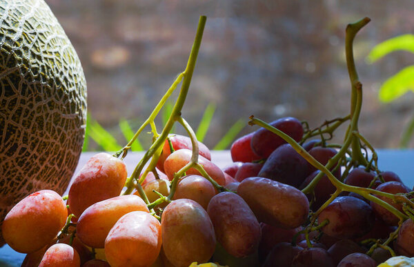                   pink grapes and figs on the table, yellow melon on one edge             