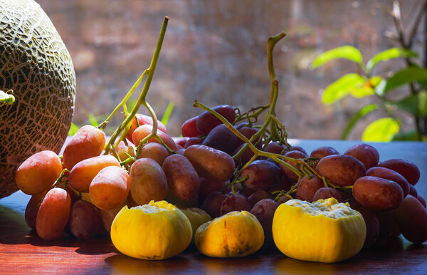                 pink grapes and figs on the table, yellow melon on one edge               