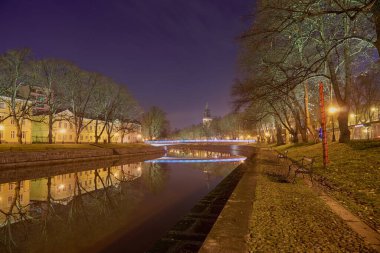 Finlandiya Turku 'daki Aura Nehri' nin gece panoramik manzarası. Arkaplanda bir katedral ve köprü kulesi vardır.