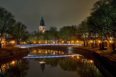 Finlandiya Turku 'daki Aura Nehri' nin gece panoramik manzarası. Arkaplanda bir katedral ve köprü kulesi vardır.