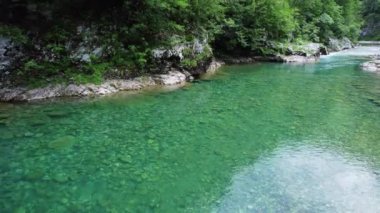 Bir vadideki temiz bir dağ nehrinin, alçak irtifadaki bir dron tarafından havadan çekilen uçurumların üzerindeki yeşil tepe örtülerinin yansıması vardır.