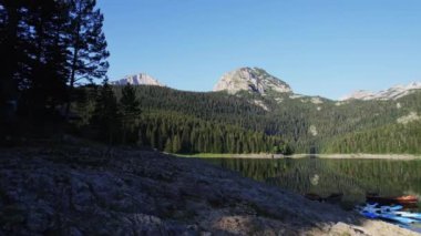 Havadan çekilen yeşil kozalaklı ormanlarla çevrili bir dağ zirvesinin altındaki buzul gölü gölün boyutunu ve gölün çevresini en az renk düzeltmesiyle gösteren ileri bir hareketle ortaya çıkar.