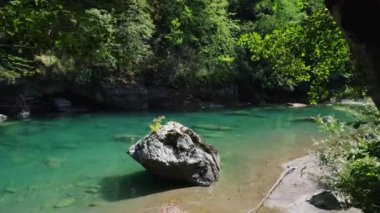 Güneşli bir günde, temiz bir dağ nehrinin üzerinde hava görüntüsü ve sudan çıkan bir kaya ve bir ağacın tepesinden başlayan hafif bir rüzgar.