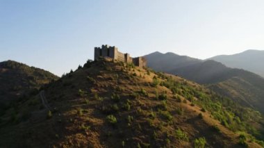 Ortaçağ kalesi Maglic, gün doğumunda bir tepede, alçalan bir dron atışı ile kaleden uzaklaşıyor. Renk düzeltmesi çok az.