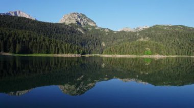 Bir dağ zirvesinin altındaki buzul gölü havadan çekilen yeşil kozalaklı ağaçlarla çevrilidir. Suyun hemen üstünde ve kıyı boyunca gölün büyüklüğünü ve gölün çevresini en az renk düzeltmesi ile gözler önüne serer.