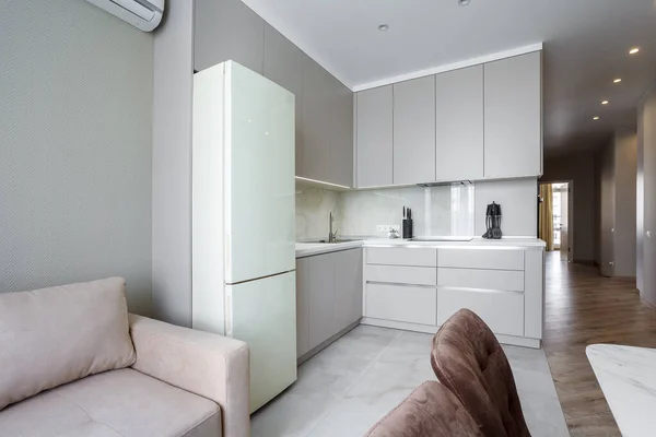 Moderne beige en grijze stijlvolle keuken met een tafel, zachte stoelen, een bank en een beige koelkast. Vloertegels en laminaat. Ingebouwde huishoudelijke apparaten Rechtenvrije Stockfoto's