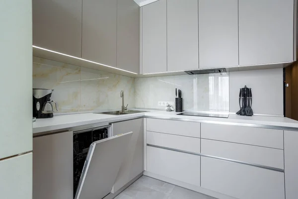 Moderne beige en grijze stijlvolle keuken met een tafel, zachte stoelen, een bank en een beige koelkast. Vloertegels en laminaat. Ingebouwde huishoudelijke apparaten Stockfoto