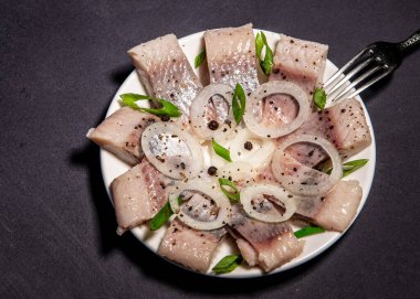 Baharatlı ve soğanlı salamura ringa filetosu. Koyu arkaplanda tuzlanmış balık. Sağlıklı doymamış yağlı yiyecekler, omega-3. Kopyalama alanı olan üst görünüm. Sağlıklı yemek.