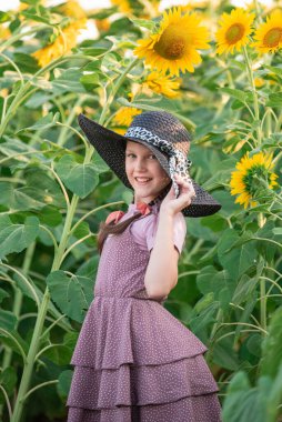 Bir ayçiçeği tarlasının arka planında örgülü saçları olan neşeli bir kız. Gün batımında portre. Sahadaki kız.