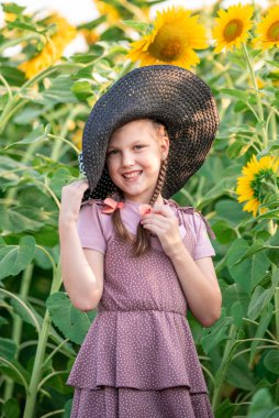 Bir ayçiçeği tarlasının arka planında örgülü saçları olan neşeli bir kız. Gün batımında portre. Sahadaki kız.