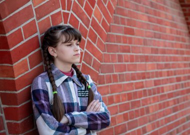 Genç bir kız tuğla duvarın yanında duruyor. Güzel tuğla duvar