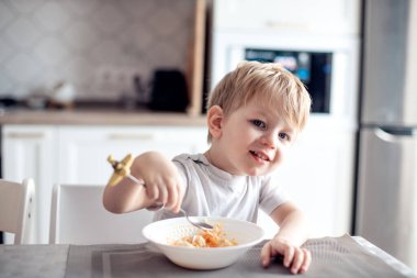 İştahlı şirin küçük çocuk mutfakta kendini yiyor. Çocuk gülümsüyor, kameraya bakıyor. Sağlıklı yiyecekler, doğal vitaminler, bebek diyeti konsepti. seçici odak