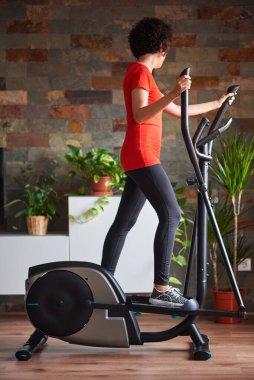 Tanımlanamayan bir kadın, evde gündüz vakti evde eliptik spor eğitmeni eğitiyor.