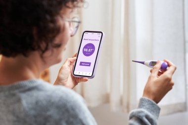 Bir kadın temel ısısını akıllı telefonunun uygulamasına kaydeder. Hamilelik için en uygun günlerin ne zaman olduğunu bilmek için bazal termometresinin ölçümleri sağ olsun.