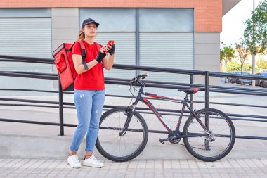 Sokakta akıllı telefon kullanan bisikletli bir teslimatçı kız.