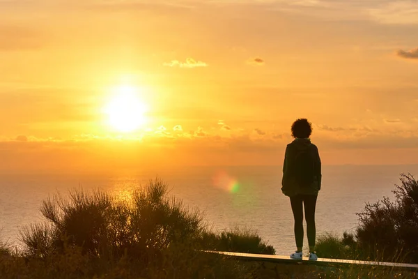 Arkadan gelen yürüyüşçü kadın denizin üzerinden güneşin doğuşuna bakıyor. — Stok fotoğraf