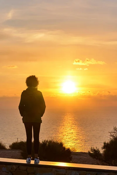 Arkadan gelen yürüyüşçü kadın denizin üzerinden güneşin doğuşuna bakıyor. — Stok fotoğraf