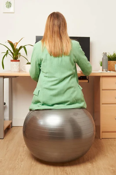 Evden çalışan tanınmayan bir kadın, fitness topunu sandalye olarak kullanıyor.