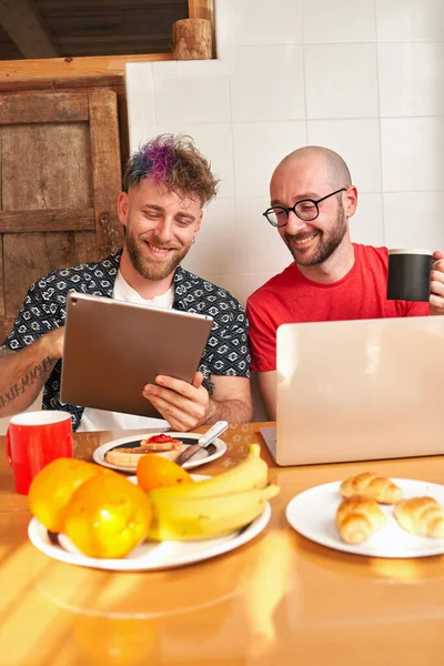 Pareja de gays en la cocina desayunando con el portátil —  Fotos de Stock