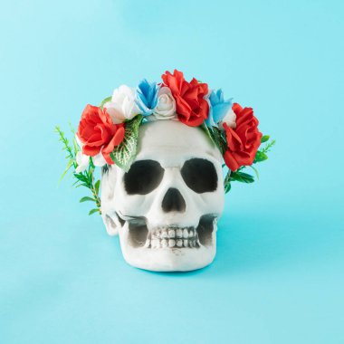İnsan kafatasında güzel, taze bir çiçek çelengi. Mavi arka planda en az Cadılar Bayramı konsepti