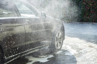 Adam arabasını oto yıkamada yıkıyor. Bir adam manuel araba yıkamada araba yıkıyor.