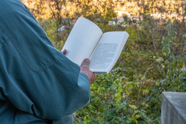 Dışarıda kitap okuyan kıdemli bir adam. Yaşlı bir adam bankta oturuyor ve kitap okuyor..