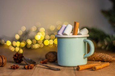 Beyaz bardaklı Noel afişi sıcak çikolatalı ve tarçın çubuklu marşmelovlu ve güzel çelenkli köknar ağacı dallı..