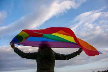 Woman holding a Gay Rainbow Flag over blue summer sky. Bisexual, gay, lesbian, transsexual symbol.	
