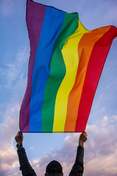 Man holding a Gay Rainbow Flag over blue summer sky. Bisexual, gay, lesbian, transsexual symbol.