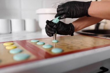 Siyah eldivenli eller, hamur işi şırıngasını sıkar. Makaron yapar.