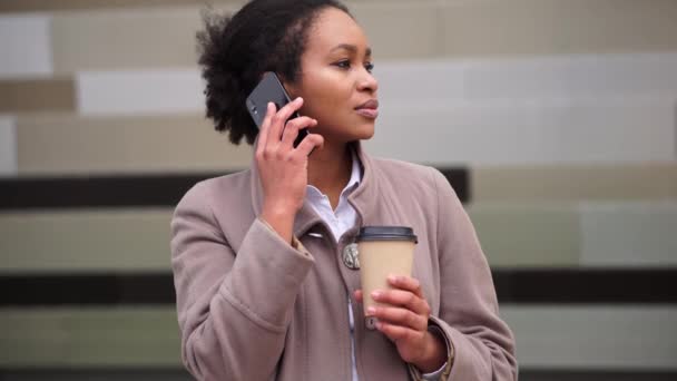 Афроамериканка з кавою, що розмовляє по телефону на вулиці. — стокове відео