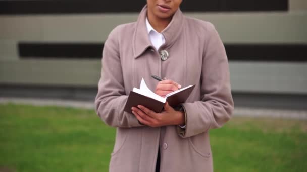 Une Afro-Américaine écrit une note dans un carnet alors qu'elle se tient debout dans la rue — Video