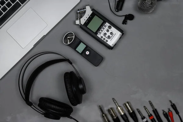 Layout bärbar dator, hörlurar, inspelare, mikrofon, kablar på en grå bakgrund. — Stockfoto