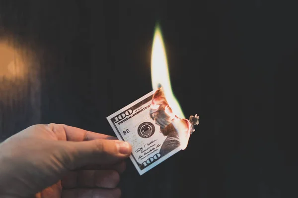Male hand close-up, holds burning money in hands, burning US dollars. Black background. The concept of inflation, a decrease in the purchase of foreign currency, and devolution.