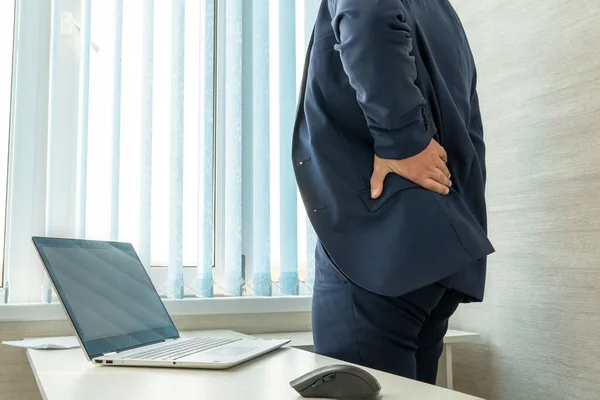 Man in desk office suffering from back pain. office worker holds his hand over his sore back. Health problems from sedentary work.